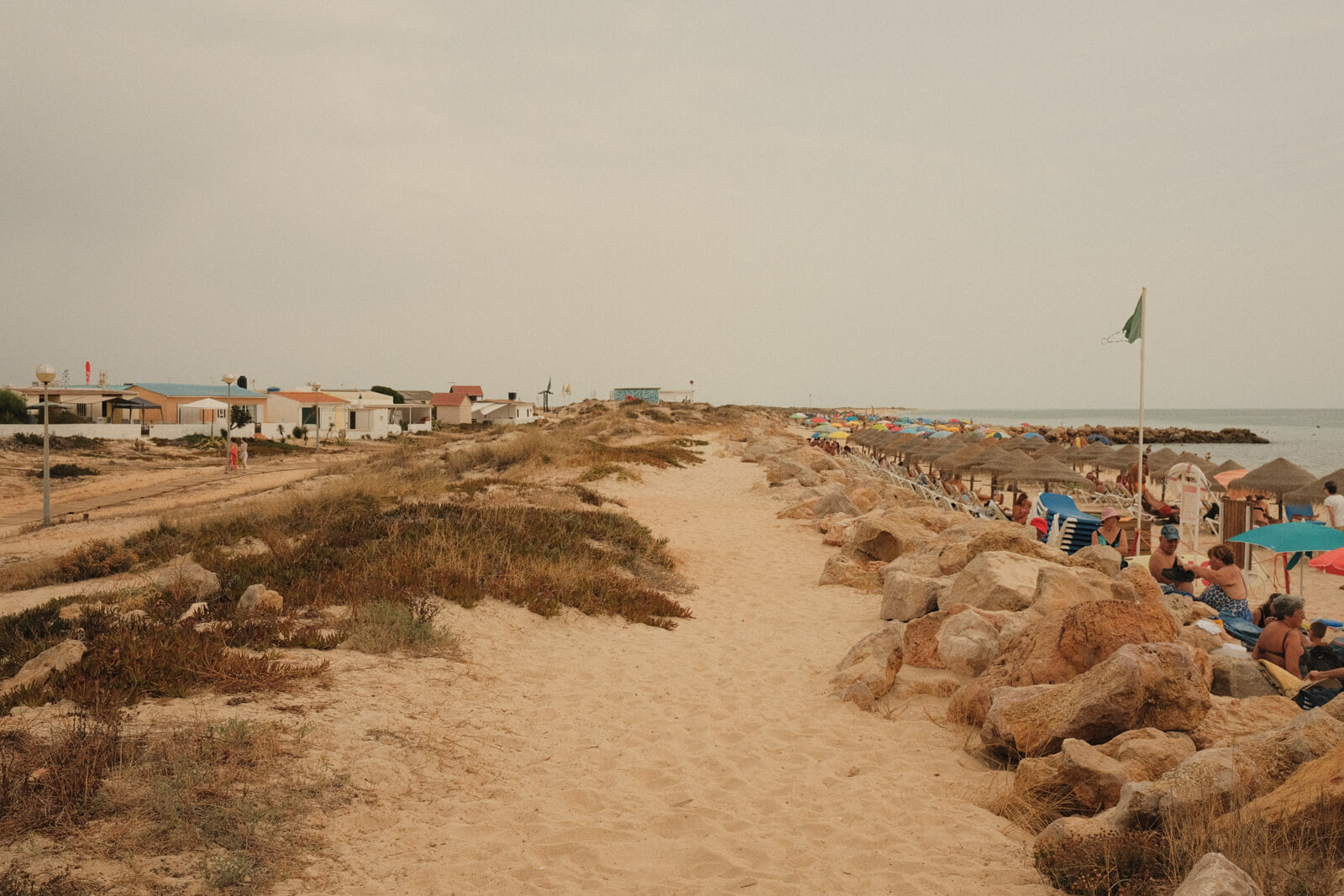 Praia do Farol busy with beachgoers and umbrellas on a hot summer day in the Algarve